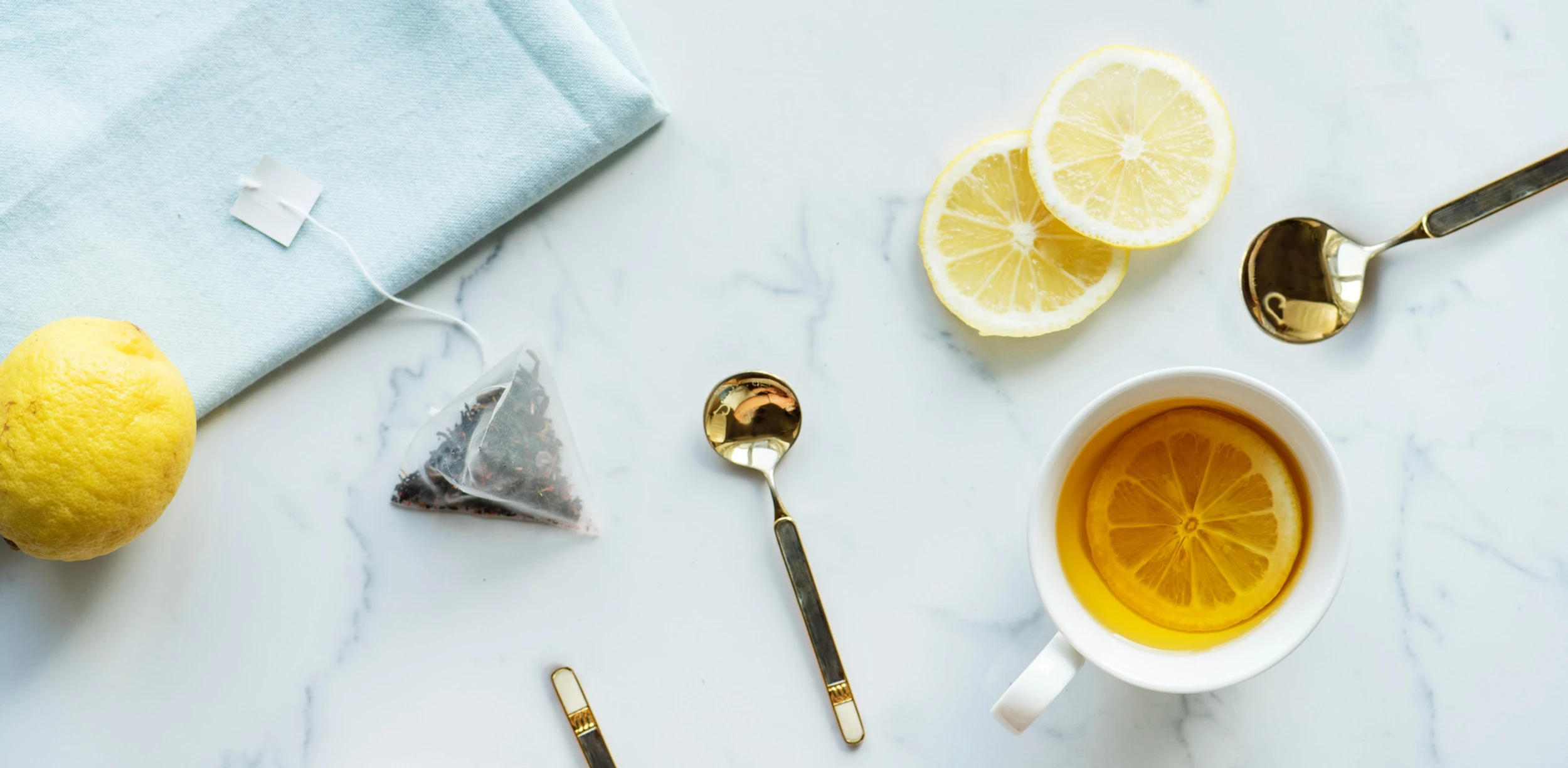 Sitronskiver, te, teposer og skjeer som ligger på et bord